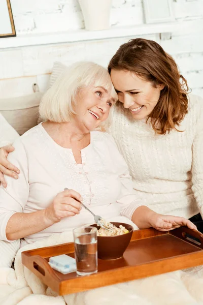 Optimistische vrouw genieten van ontbijt met oude moeder thuis — Stockfoto