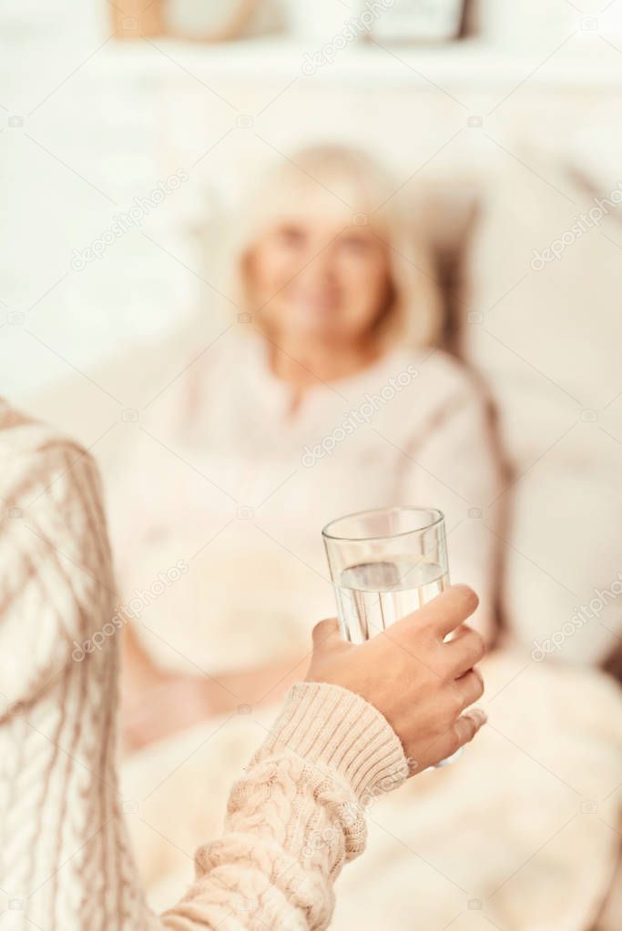 Positive woman giving glass of water for ill mother
