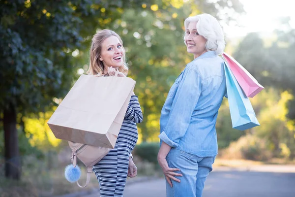 Pregnant woman demonstrating purchases with aged mother outdoors — Stock Photo, Image