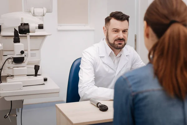 Guapo oftalmólogo agradable sentado a la mesa — Foto de Stock