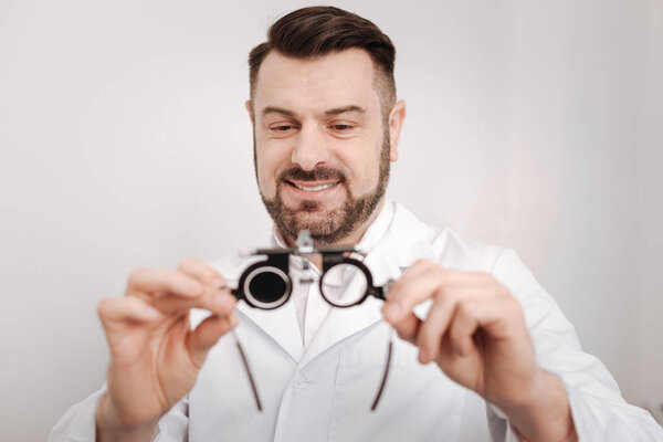 Pleasant happy doctor looking at the eye test glasses