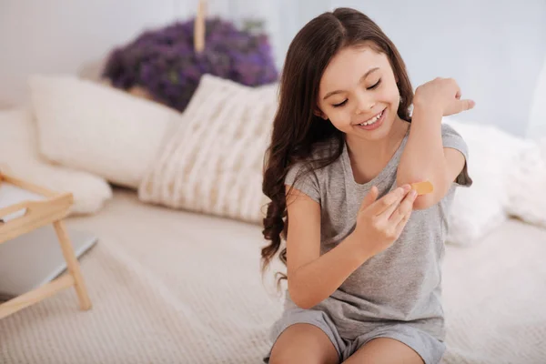 Joyful child treating her wound on the elbow at home — Stock Photo, Image