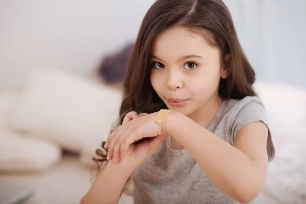 Little girl putting adhesive bandage on her injury at home — Stock Photo, Image