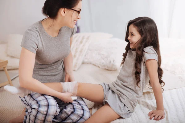 Encantado mãe bandagem filha perna em casa — Fotografia de Stock