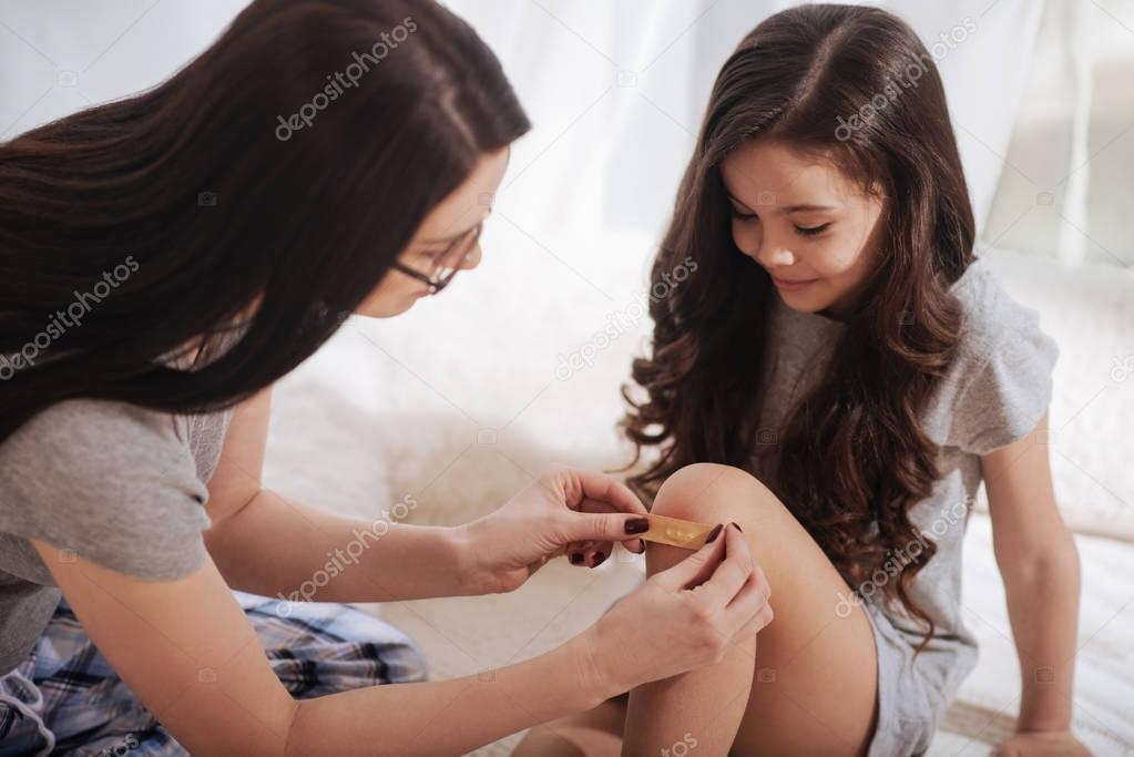Loving mother treating little daughters wound at home