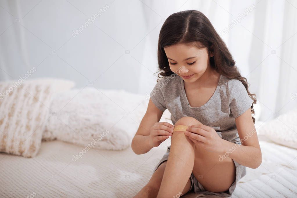 Smart child applying adhesive bandage on knee at home