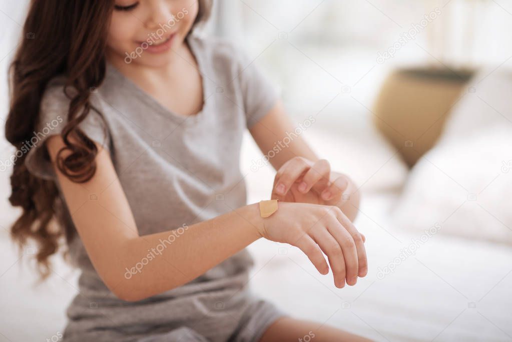Concentrated girl putting aid plaster on her cut at home