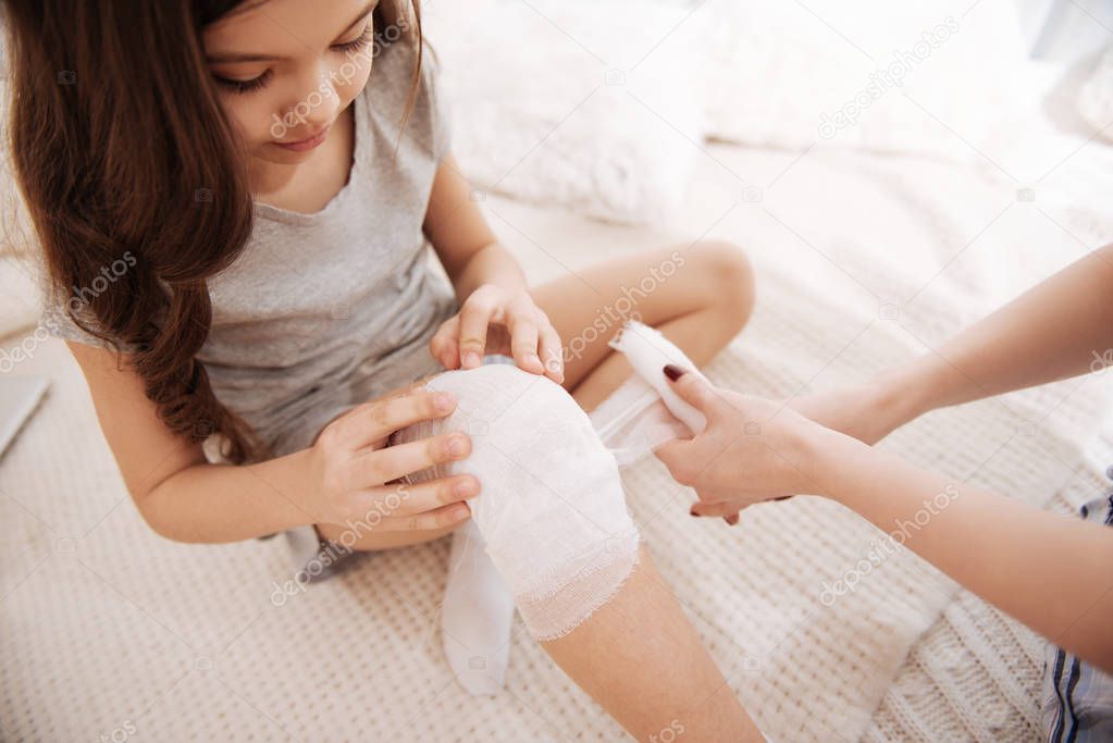 Focused little girl taking part in bandaging her injury at home