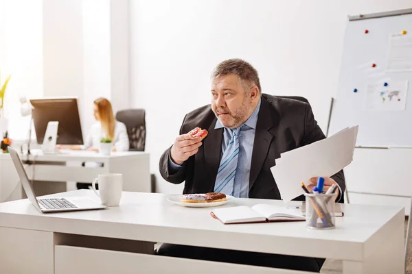 Trabalhador cansado excessivo tendo um lanche insalubre — Fotografia de Stock