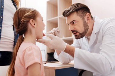 Küçük kızın boğazını inceleyerek dikkatli çocuk doktoru