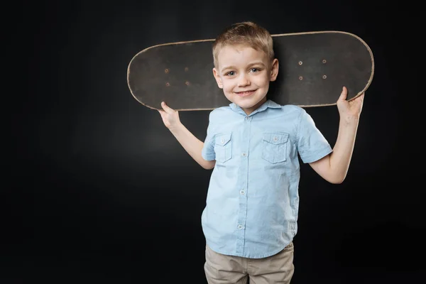 Sorridente ragazzo mantenendo skateboard dietro la testa — Foto Stock