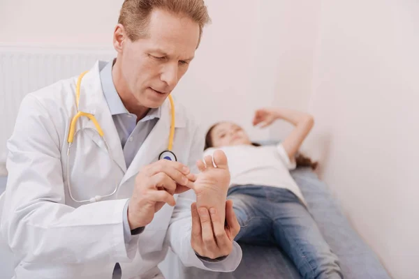 Especialista preciso inteligente que estuda cuidadosamente pacientes pés — Fotografia de Stock