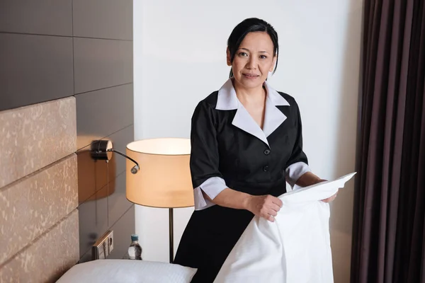 Pleasant Asian hotel maid holding a sheet — Stock Photo, Image