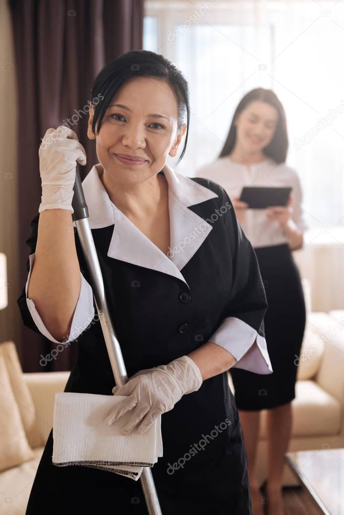 Nice delighted hotel maid holding a mop