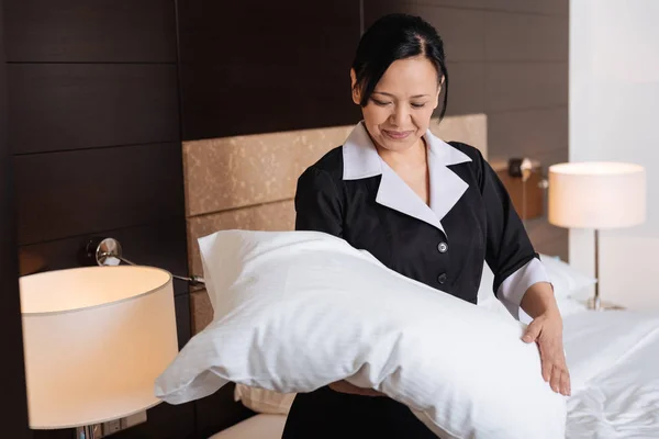 Trabajo duro positivo sirvienta del hotel mirando la almohada —  Fotos de Stock