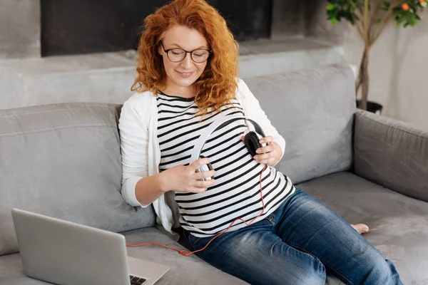 Vackra blivande modern att sätta hörlurar över baby bump — Stockfoto