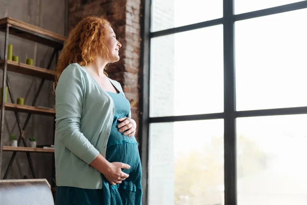 Smilende vordende mor ser ut av vinduet – stockfoto