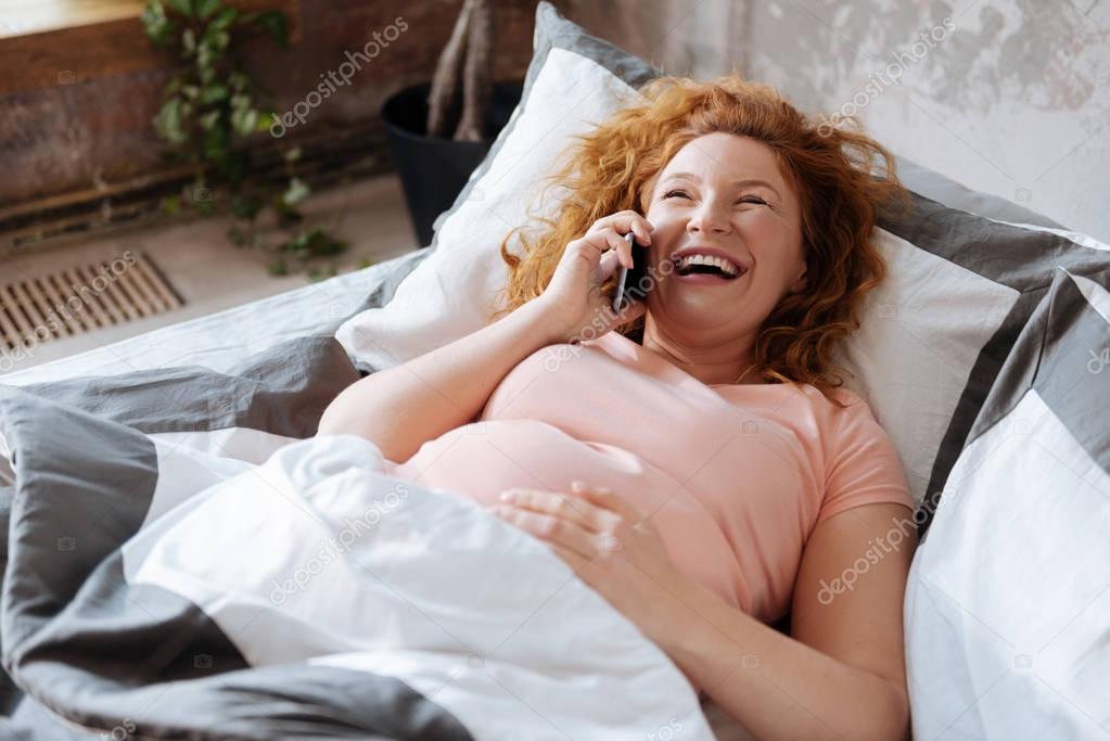 Mother-to-be talking on phone in bed and laughing