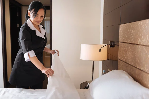Agradable doncella de hotel positivo mirando a la cama — Foto de Stock