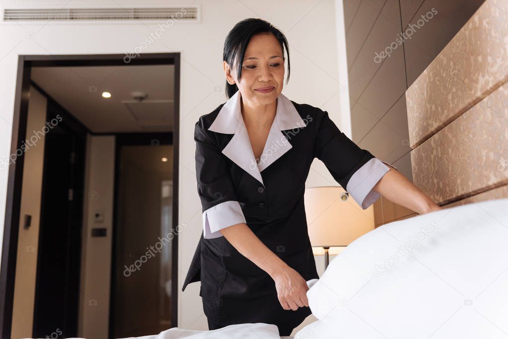 Hard working professional hotel maid arranging the pillow
