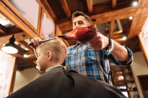 Cabeleireiro experiente agradável segurando um secador de cabelo — Fotografia de Stock