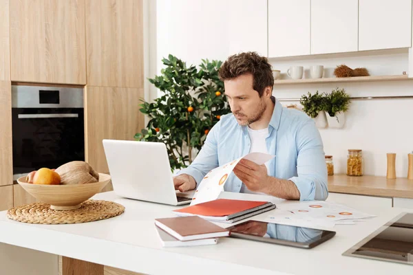 Serious man looking working on a laptop and checking documents — Stock Photo, Image