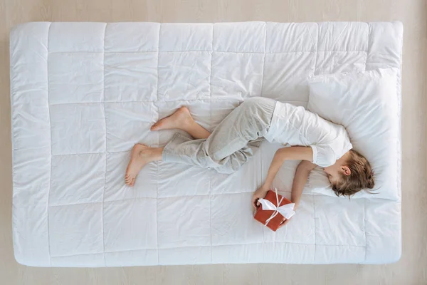 Хлопчик відпочиває на ліжку тримає подарунок — стокове фото
