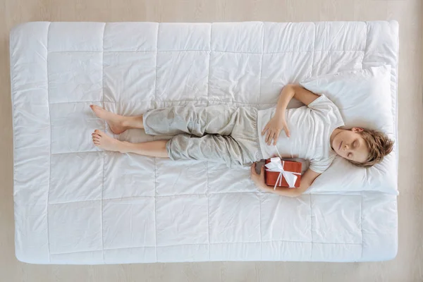 Anak beristirahat di tempat tidur sambil memegang hadiah — Stok Foto