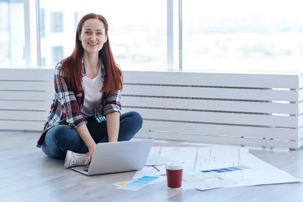 Trevlig glad kvinna som sitter nära hennes utkast — Stockfoto