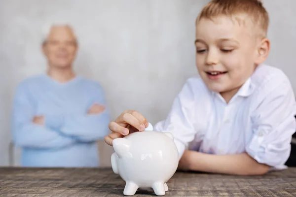 Netter aufgeregter Junge legt eine Münze in ein Sparschwein — Stockfoto