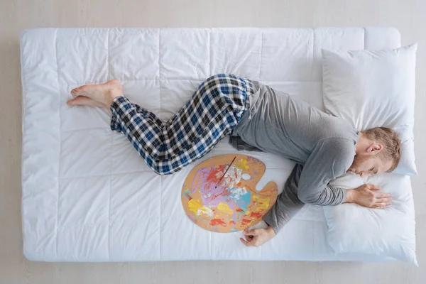 Creativo buen hombre durmiendo con una paleta de artistas — Foto de Stock