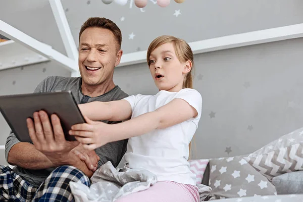 Lively girl and her parent playing with the tablet