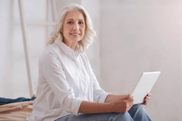Mujer mayor agradable sosteniendo un ordenador portátil — Foto de Stock