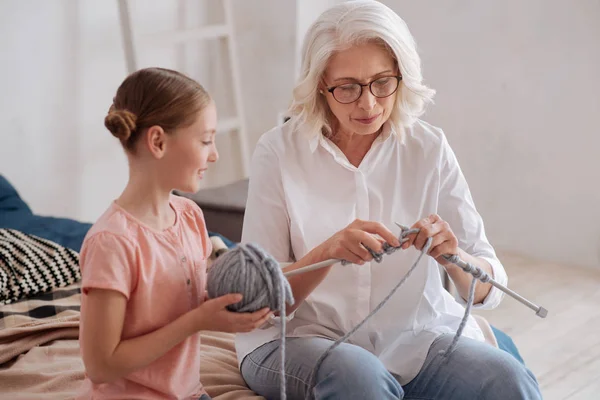 Positive nice woman teaching her granddaughter to knit — Stock Photo, Image