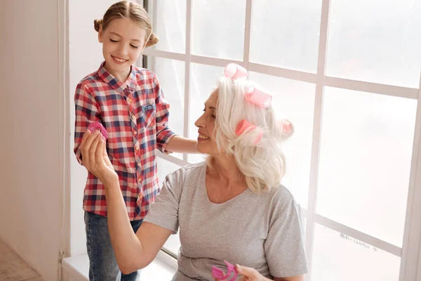 Happy aged woman giving a hair roller to her granddaughter — Stock Photo, Image