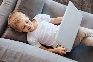 Yaratıcı serin çocuk onun dizüstü bilgisayar ile bir kanepede rahatlatıcı