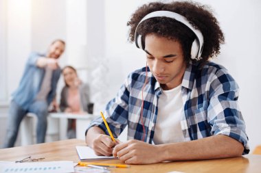 Dedicated young man listening to music while studying clipart
