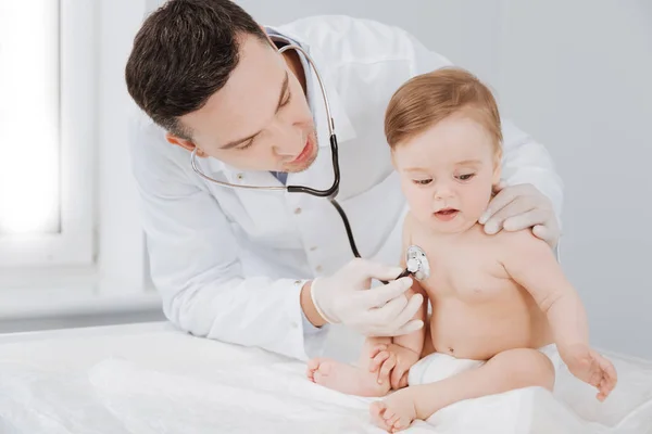 Precise competent pediatrician checking toddlers lungs — Stock Photo, Image