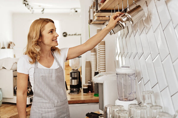 Красивая бариста регулирует молоко пенящееся кувшины на стене
