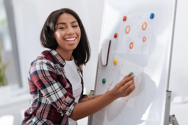 Joyful young woman putting visual materials on the whiteboard