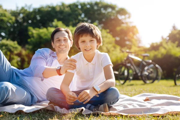 Handsome young kid sitting on the grass with his dad