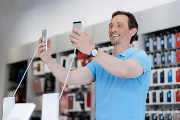 Волнующий мужчина делает селфи с двумя телефонами в магазине — стоковое фото