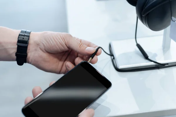 Escalar olhar para cima em mãos masculinas conectando fones de ouvido em smartphone — Fotografia de Stock