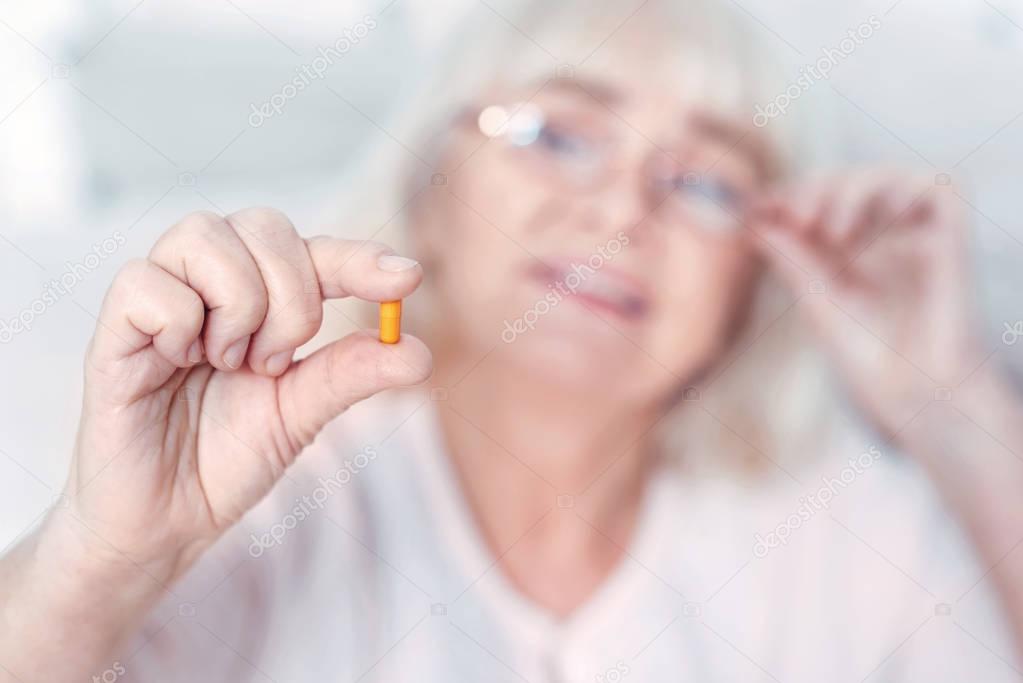 Curious elderly woman viewing pill at home