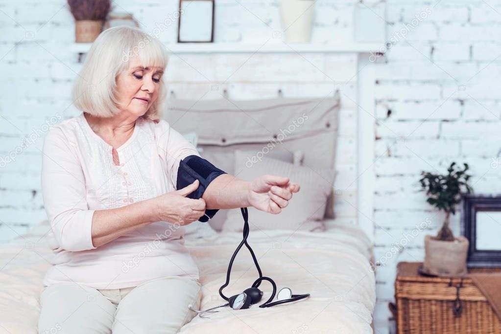 Confident elderly lady measuring blood pressure at home