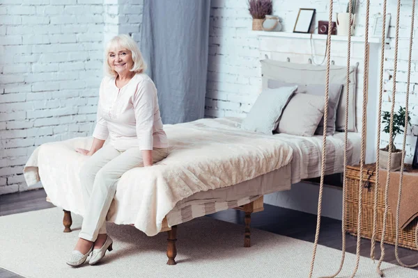 Mujer anciana alegre sentada en el dormitorio — Foto de Stock