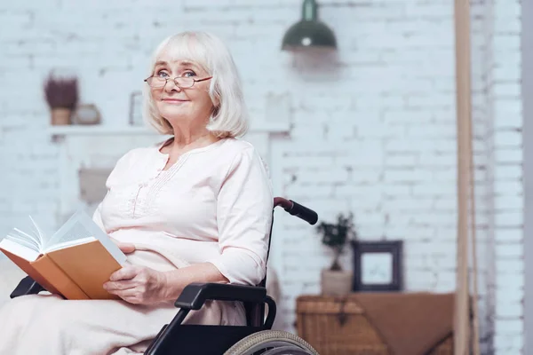 Alte behinderte Frau liest Buch im Rollstuhl zu Hause — Stockfoto