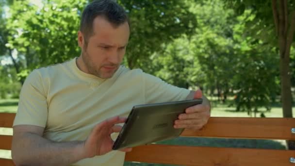 Positive man sitting in the park with the laptop — Stock Video