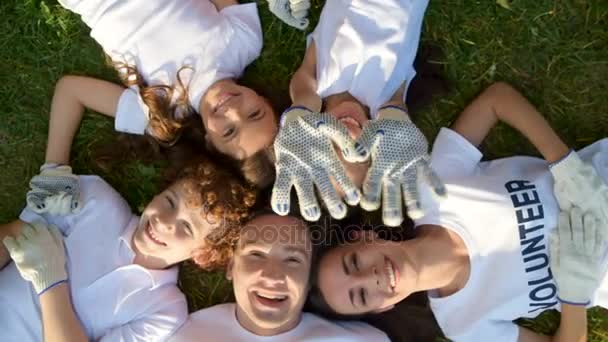 Fille agitant tandis que le groupe de bénévoles se détendre sur l'herbe — Video