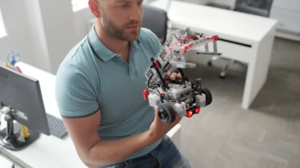 Сосредоточенный молодой человек разрабатывает робота за работой — стоковое видео